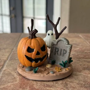 Painted pumpkin scene sculpture: an orange jack-o’-lantern, a small ghost and an RIP gravestone on a round base