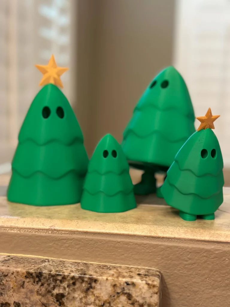 Green Christmas trees with hidden legs, two with gold stars, on a kitchen ledge
