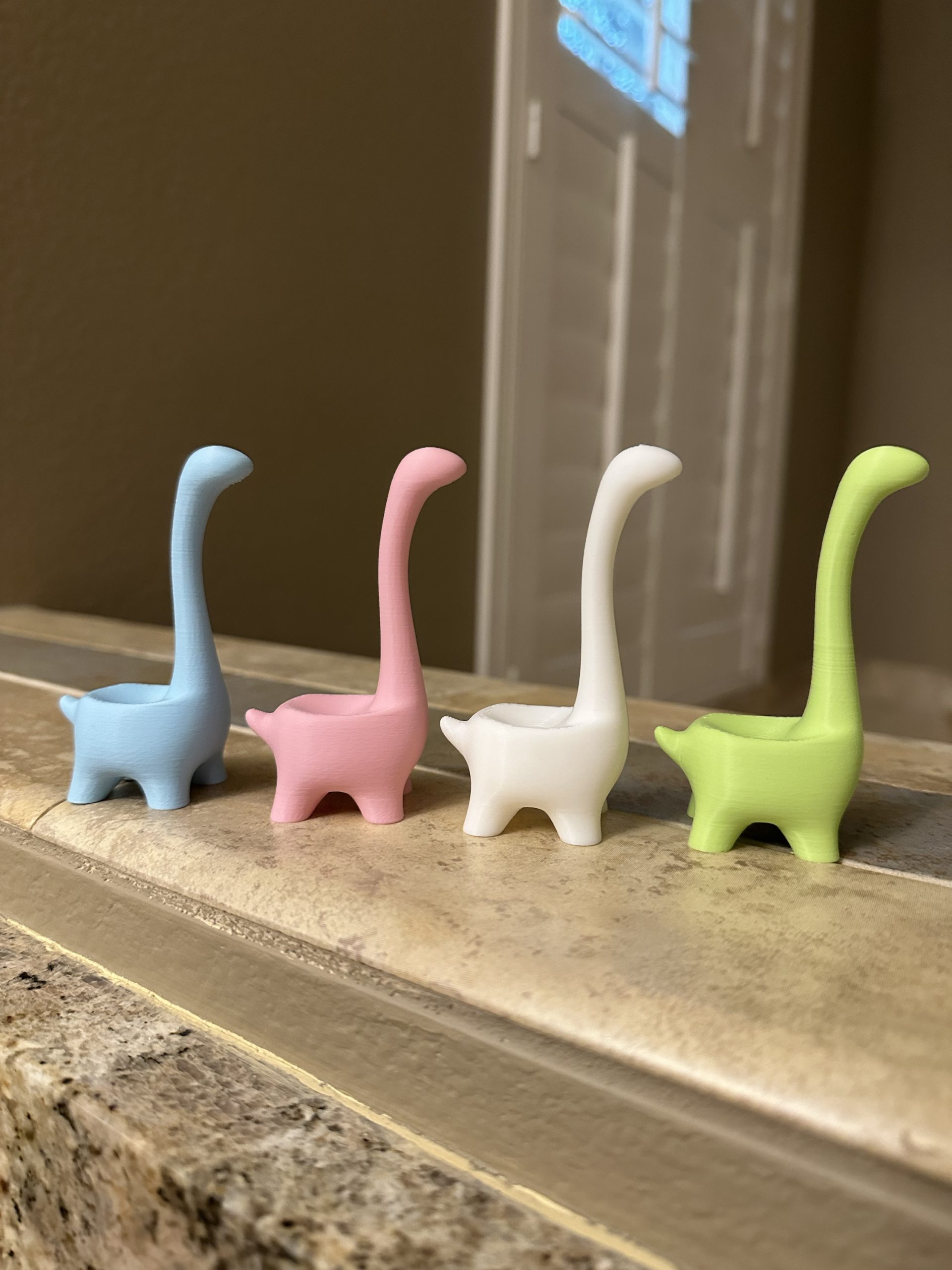 Ringosaurus ring holders in light blue, light pink, white and light green, in a row