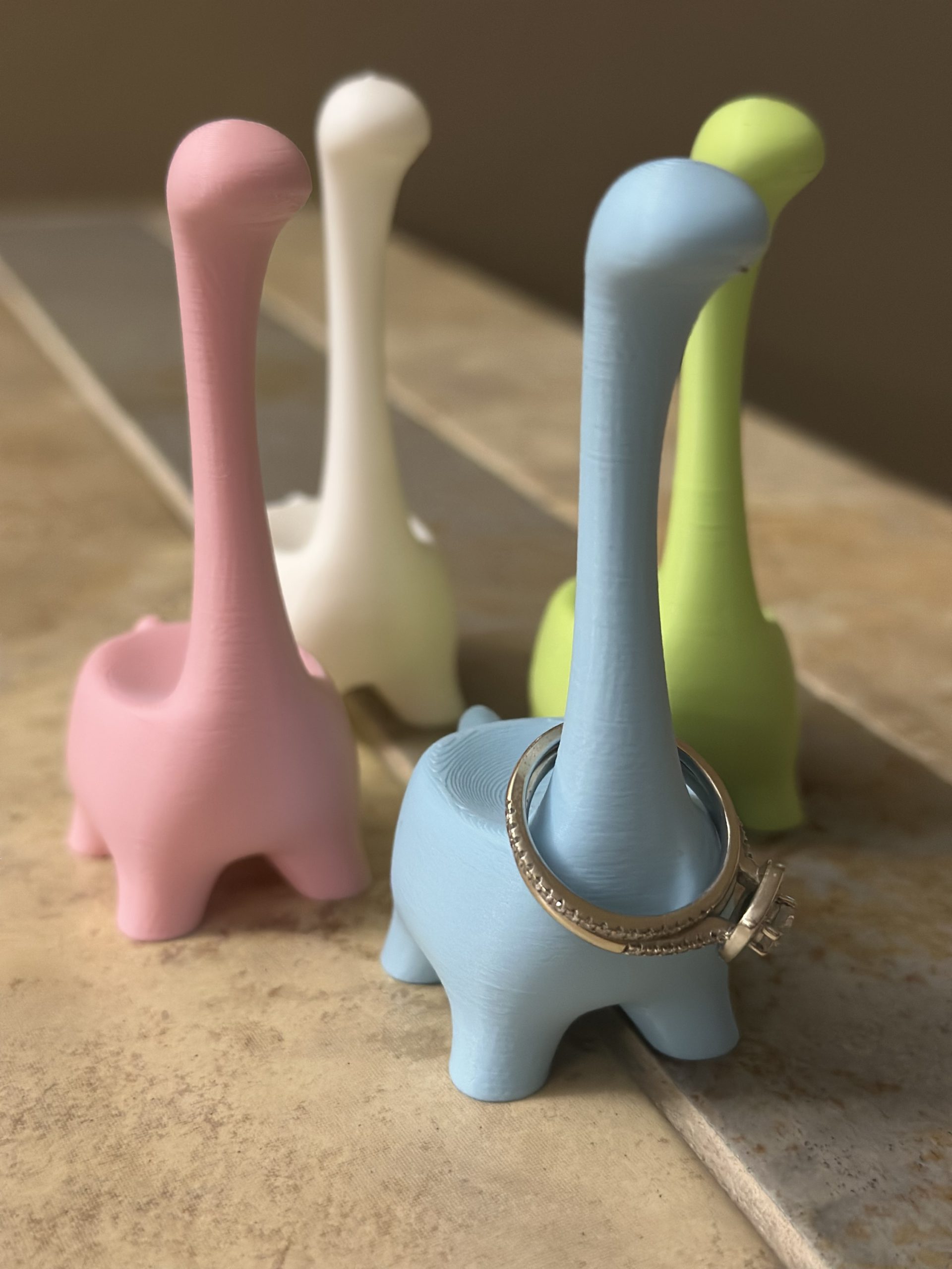 Ringosaurus ring holders in light pink, white, light blue and light green, with rings on the blue one