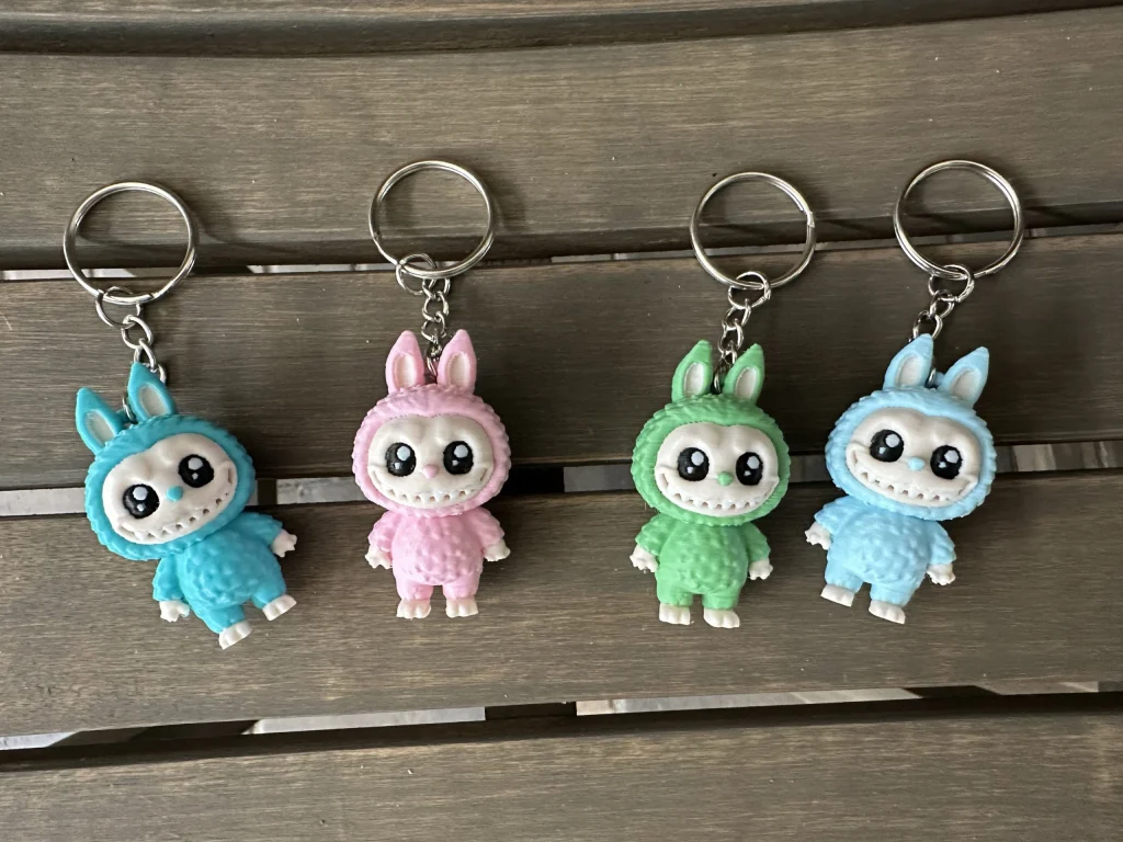 Doll keychains in teal, light pink, mint green and light blue, hanging in a row