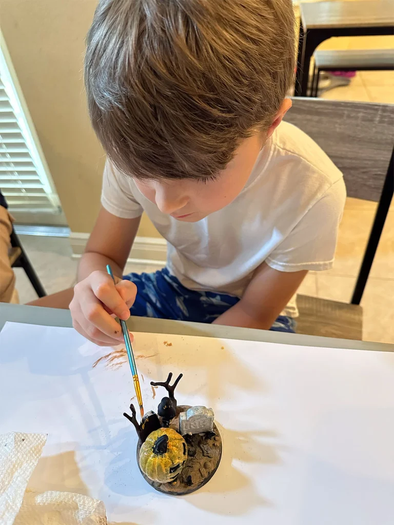A young member of the family painting a small 3D-printed pumpkin scene